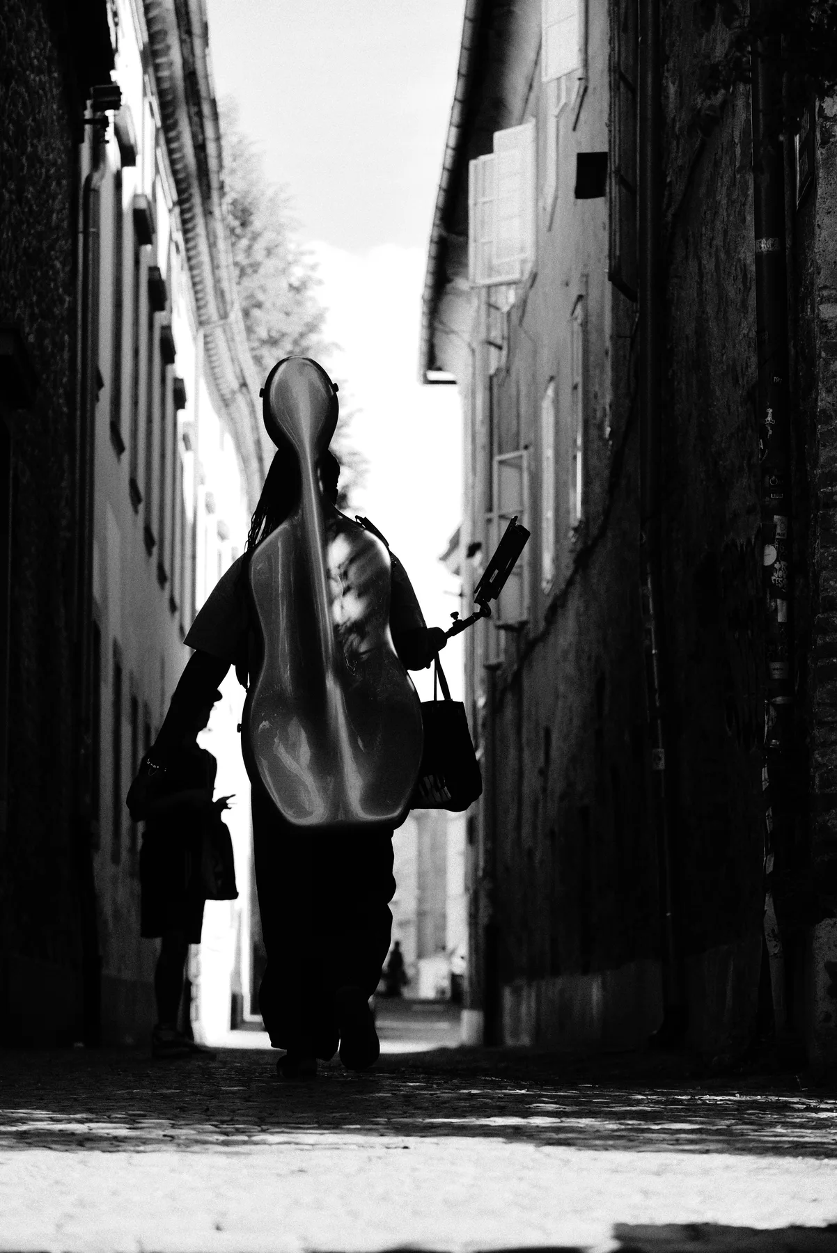 A black-and-white view of a musician walking away with an instrument case.